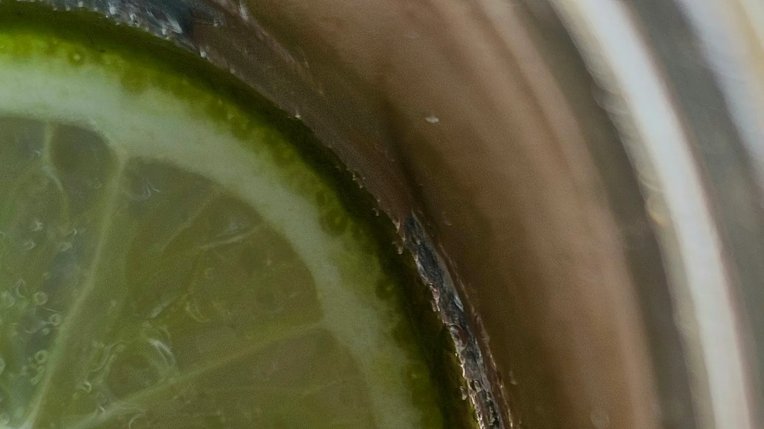 A macro view of a lime slice suspended in a glass of sparkling water with rising bubbles