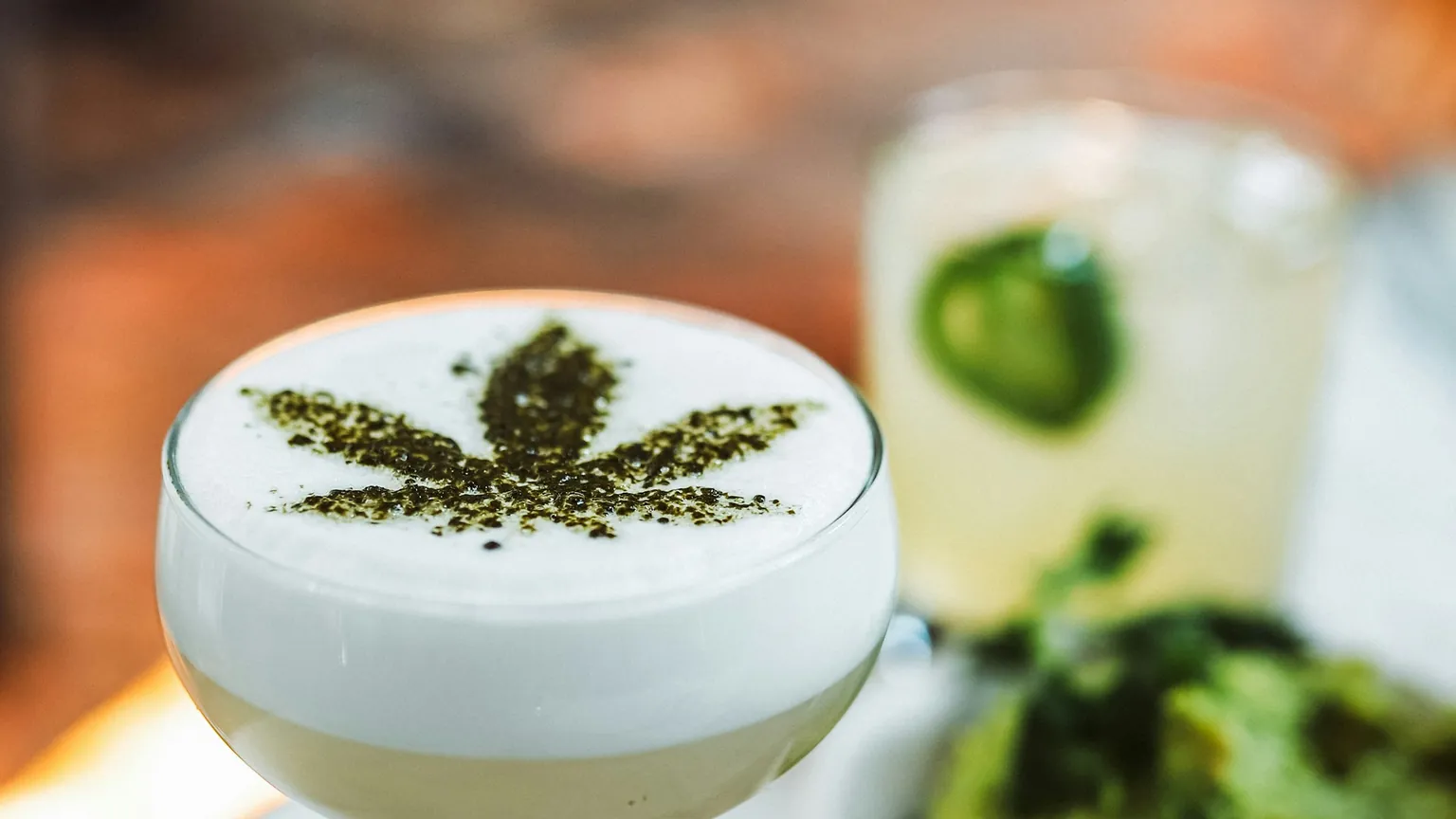 An infused mocktail in a coupe glass topped with a cannabis leaf dusted onto the foam