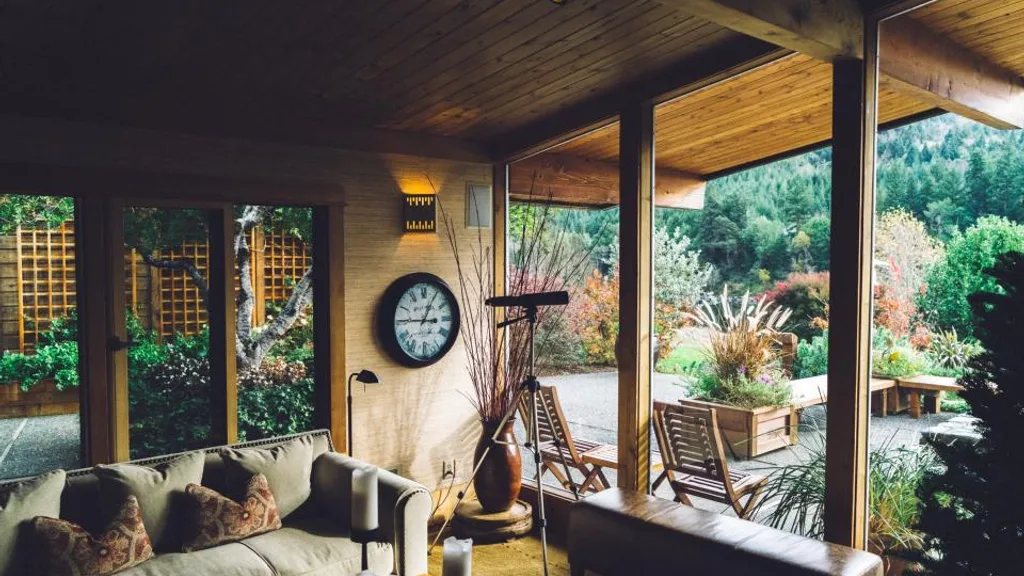 A cozy living room with a sofa, candles, and a wall clock opening onto a garden