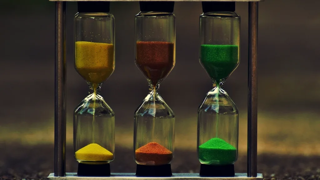 Three sand timers with yellow, red, and green sand standing in a metal frame