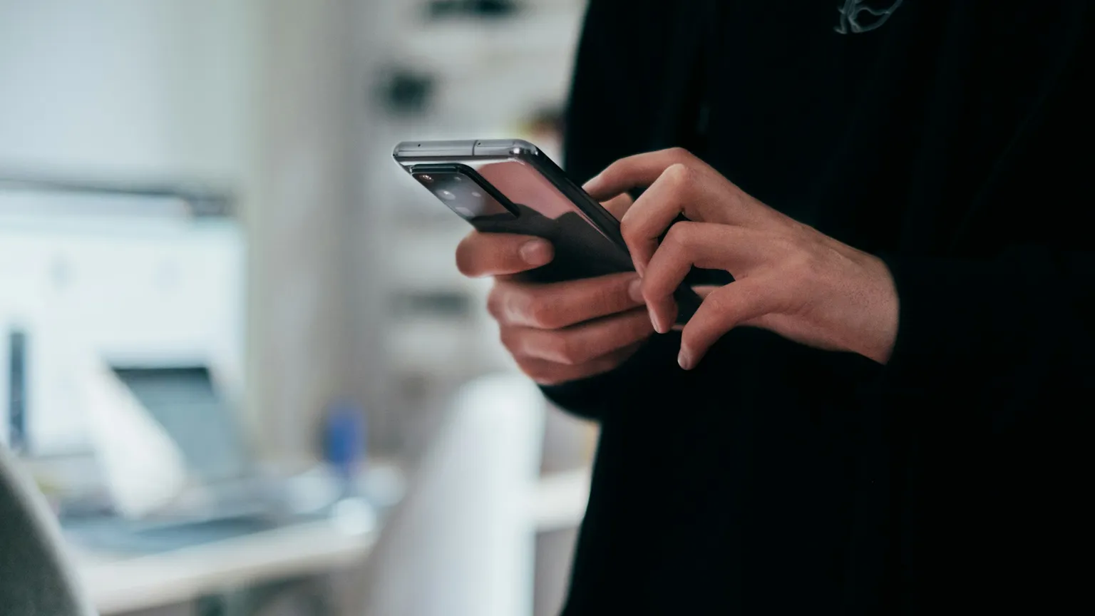 Close-up of a person placing an order on a smartphone with a laptop blurred behind