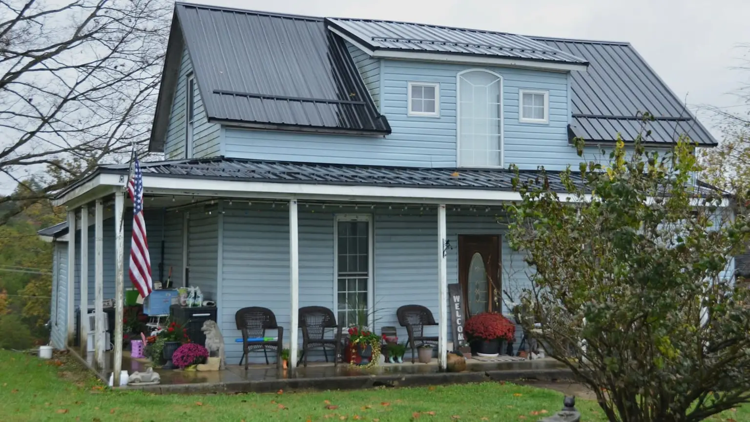 A rural New England farmhouse with a covered front porch on an overcast autumn day