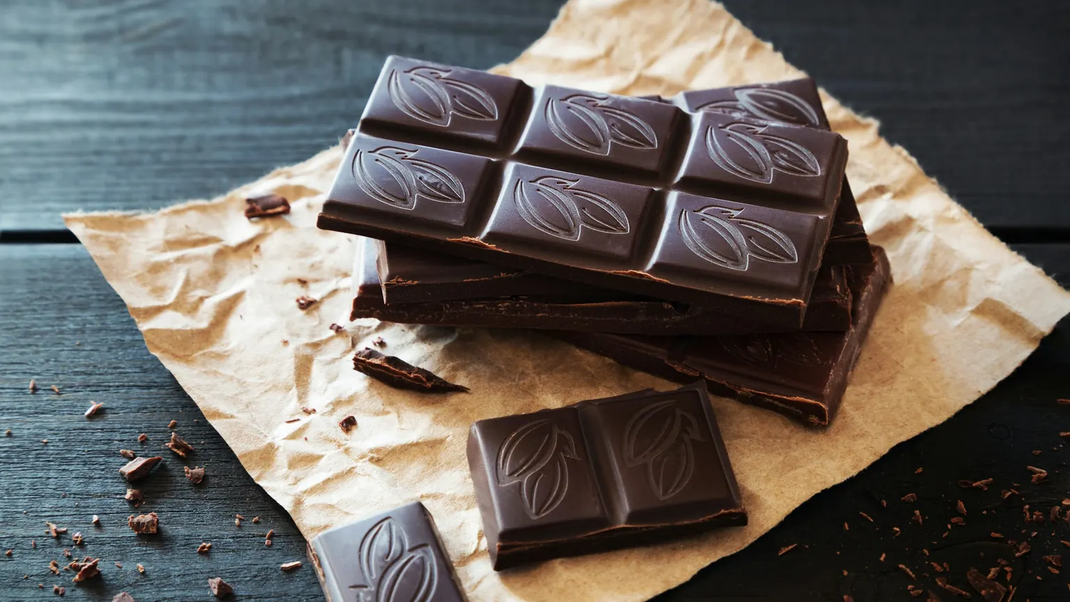 Stacked squares of dark chocolate on crumpled kraft paper over a dark wooden table