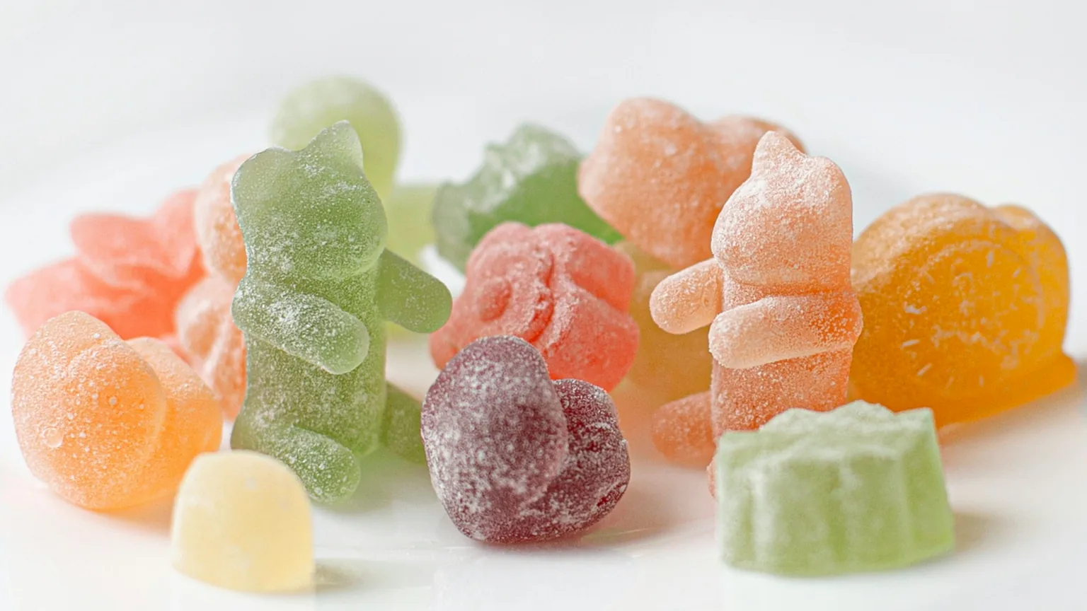 Soft sugar-coated gummies in pastel colors arranged on a white surface