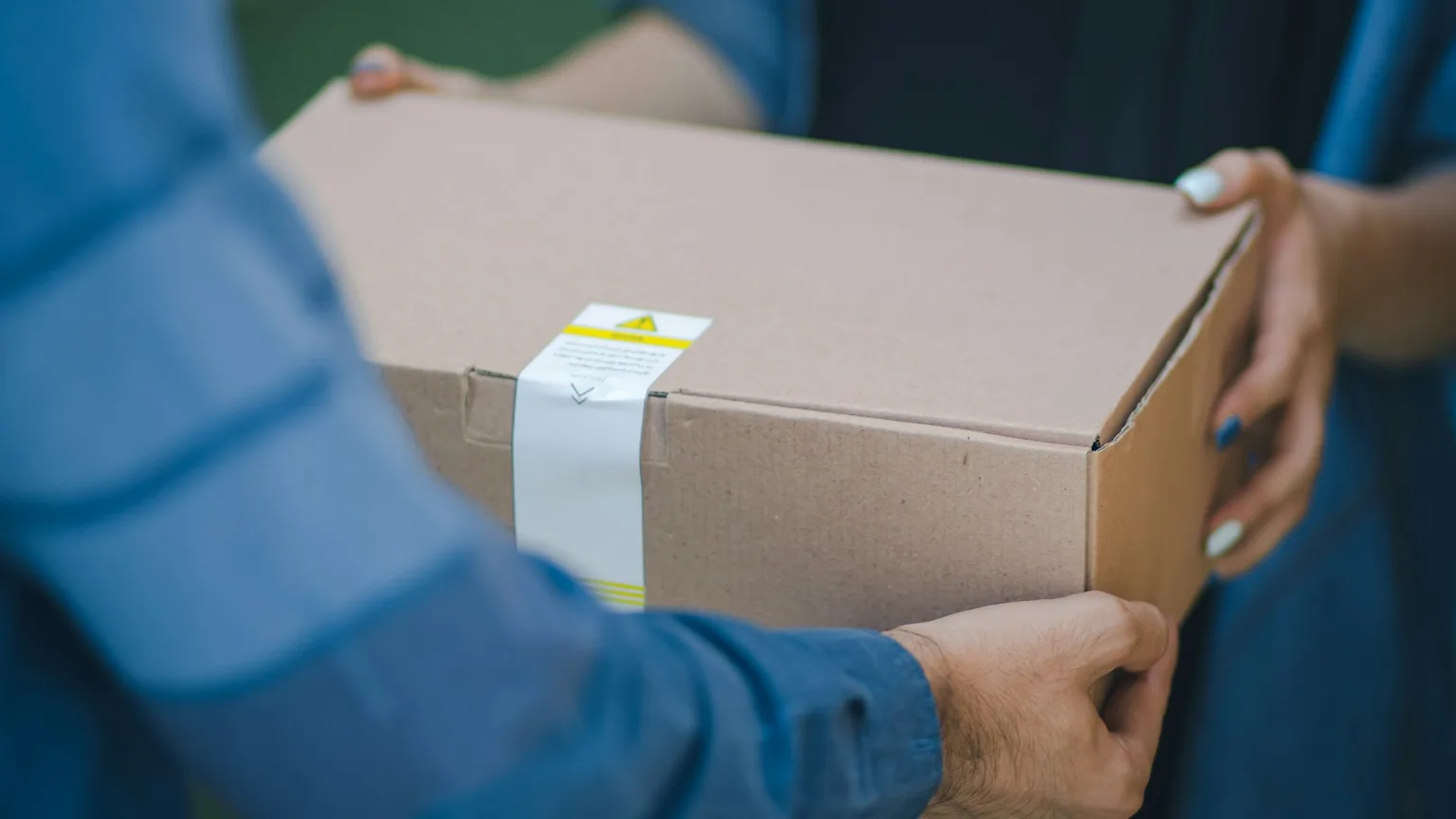 A driver handing a plain sealed cardboard package directly to a customer at the door