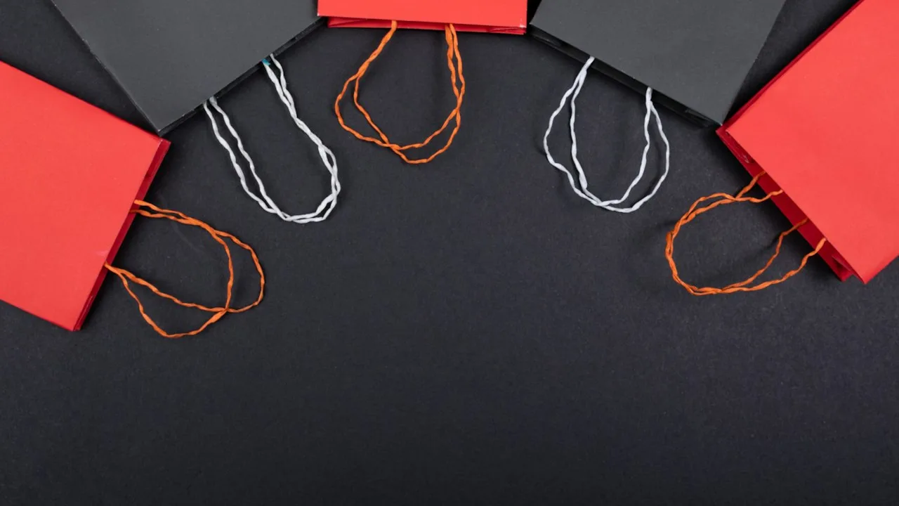 Red and black paper shopping bags with rope handles laid out on a dark surface