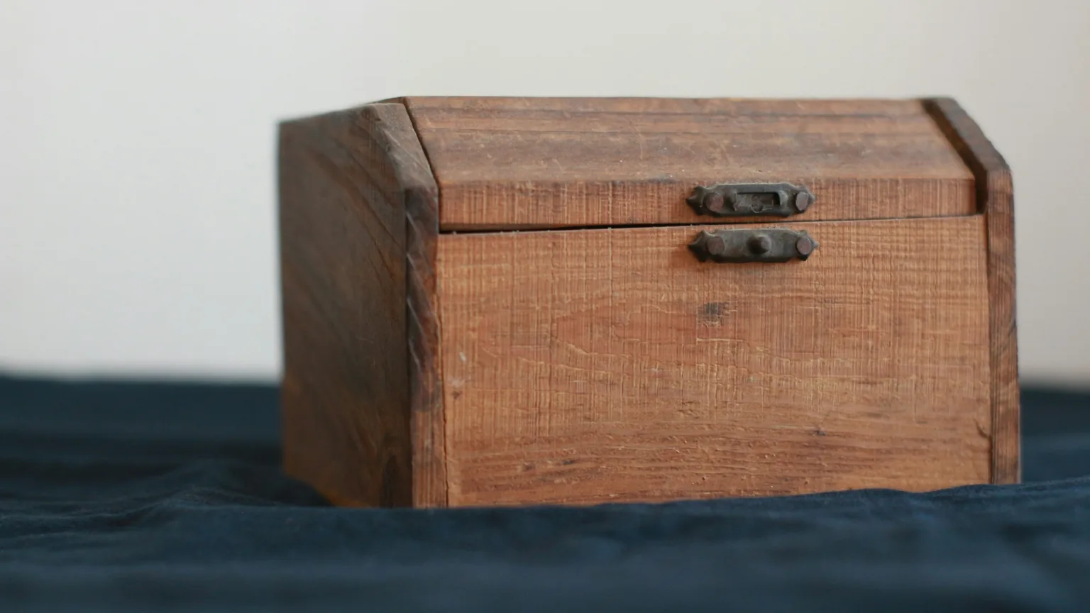 A latched wooden storage box closed on a dark cloth against a plain pale wall