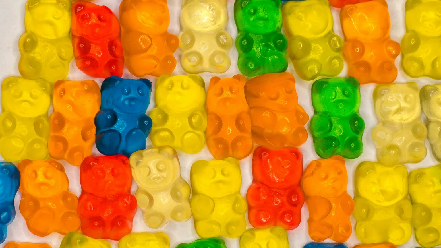 Rows of brightly colored gummy bears laid out in a grid on a white surface