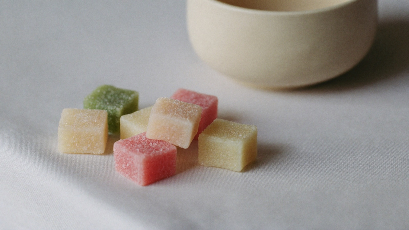 A few sugar-dusted gummies resting on a pale linen surface beside a ceramic bowl