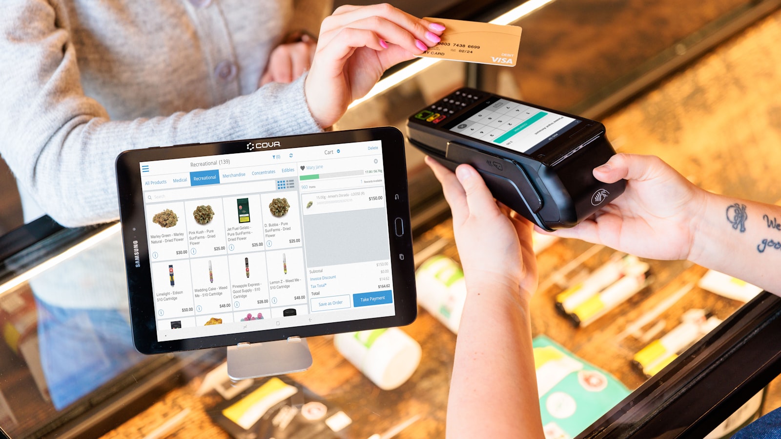A customer paying by card at a dispensary counter beside a menu tablet